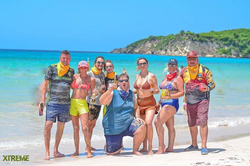 A group of people on a beach with clear blue water and a distant rocky island. 5