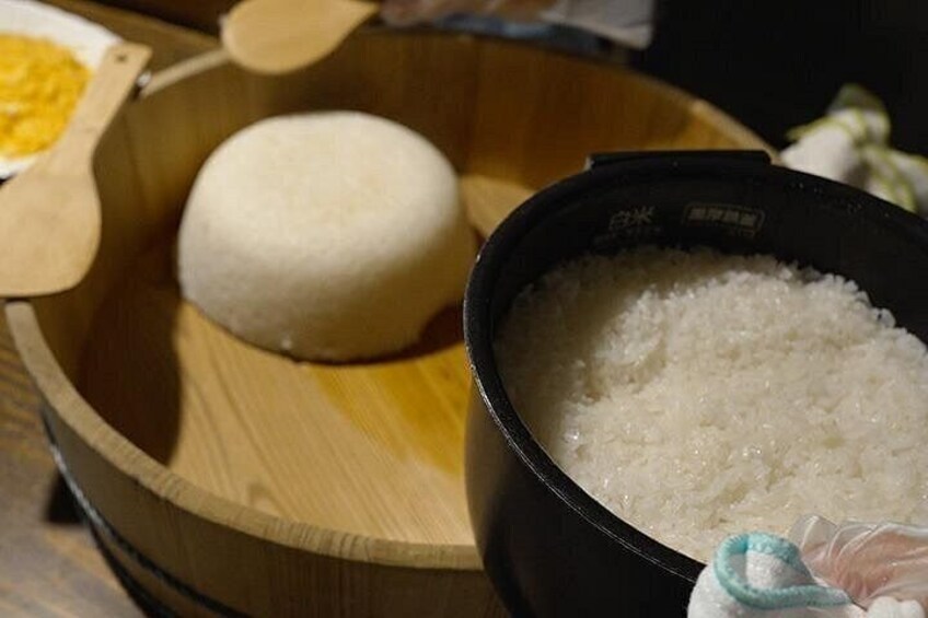 A wooden bowl containing a white rice ball and a black bowl filled with white rice. 5