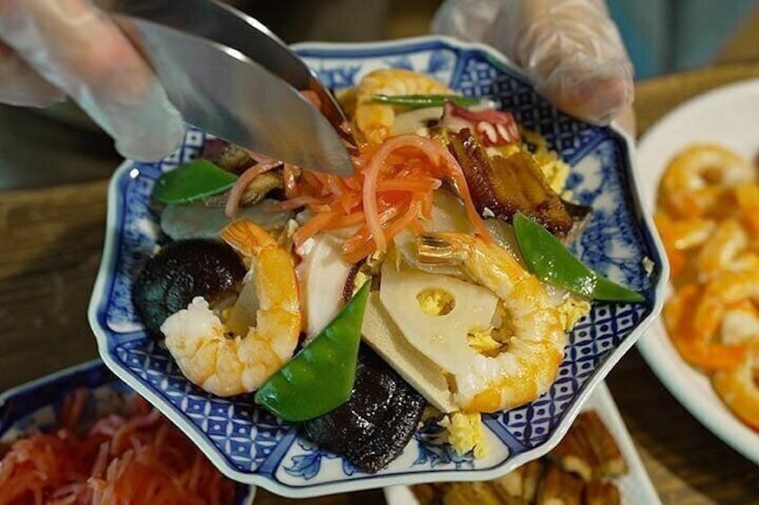 A person serving a dish with shrimp, vegetables, and possibly seafood on a blue patterned plate. 1