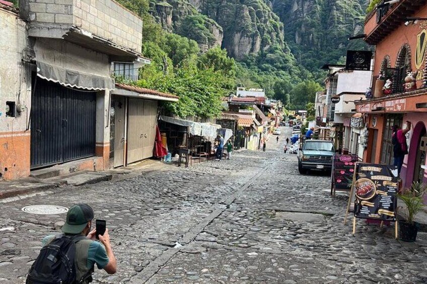 Une rue pavée dans une région montagneuse, avec des boutiques et une personne prenant une photo. 2