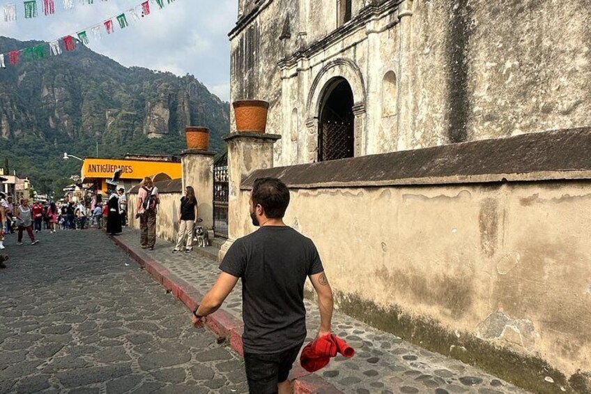 A cobblestone street with a man walking, a building with a sign reading "ANTIGUERAS," and mountains in the background. 2