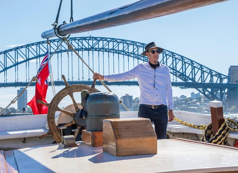 A person on a boat with a steering wheel, a flag, and a large bridge in the background. 5