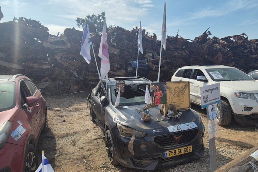 A damaged car with flags, a white SUV, and a red car in a junkyard. 3