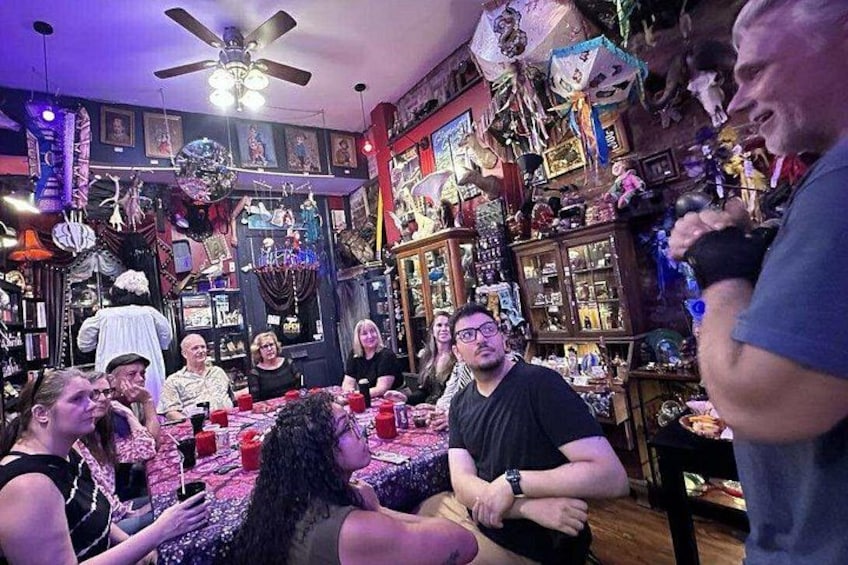 A group of people seated around a table in a room filled with various items and decorations. 1