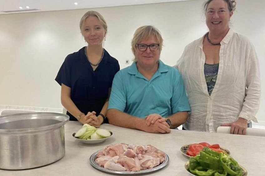 Trois personnes se tiennent dans une cuisine, devant un plan de travail sur lequel se trouvent du poulet cru, des légumes et une casserole. 1