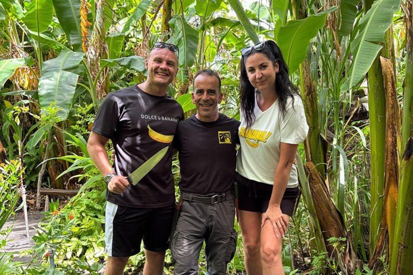 Three people standing in a lush, green environment with banana plants. 2