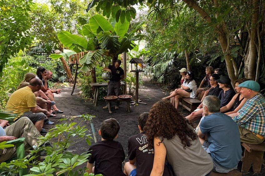 Eine Gruppe von Personen sitzt draußen in einem Garten und lauscht einem Redner. 1