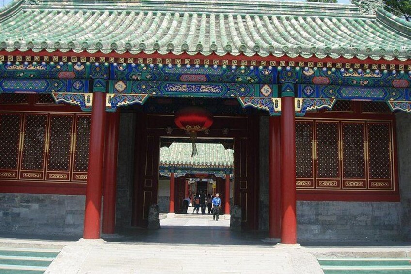 Une porte chinoise traditionnelle, ornée de motifs complexes aux couleurs bleu et or, avec des piliers rouges et un toit recouvert de tuiles. 1