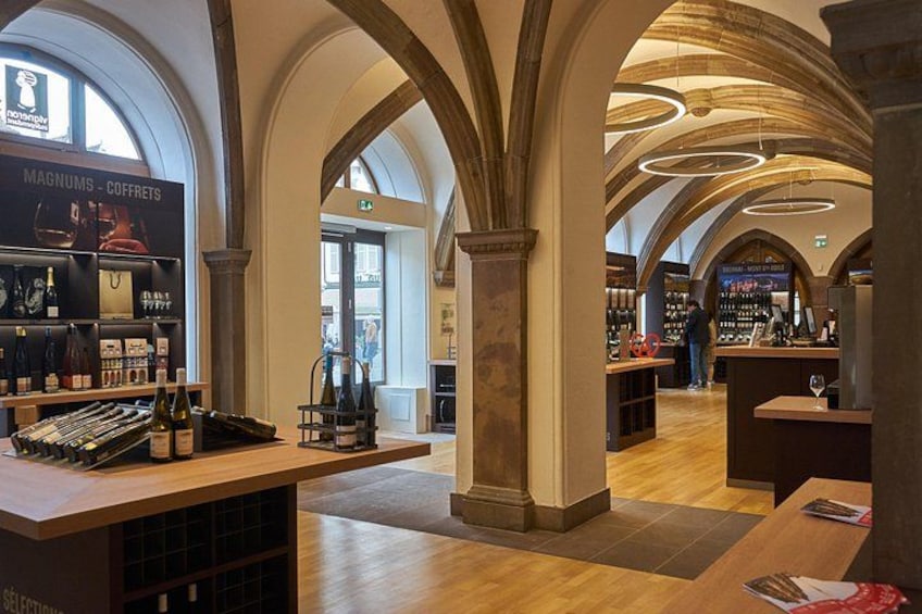 An interior with arched ceilings, wooden flooring, and shelves displaying wine bottles. 3