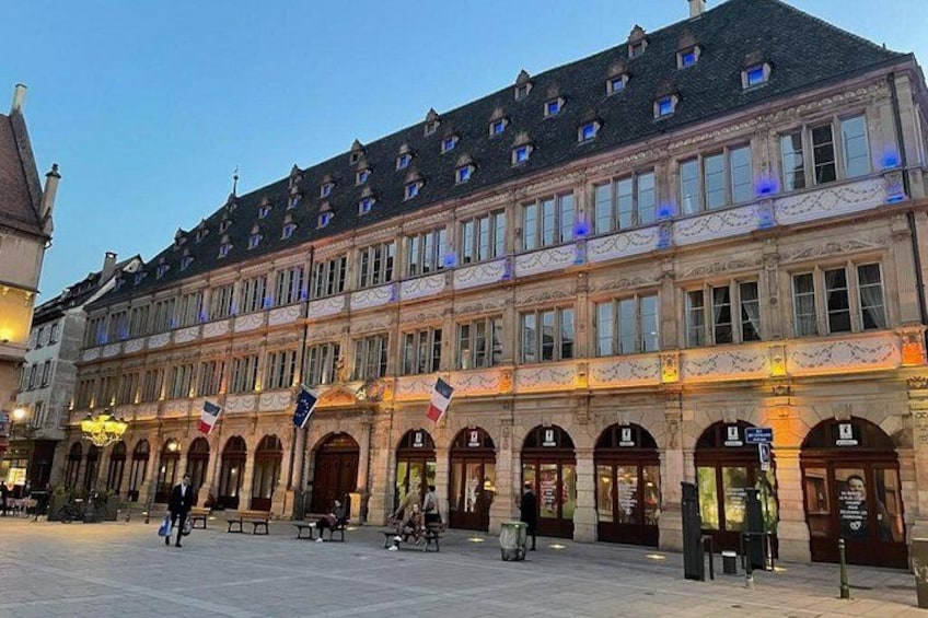 A historic building with multiple arches and flags, a paved square, and benches. 4