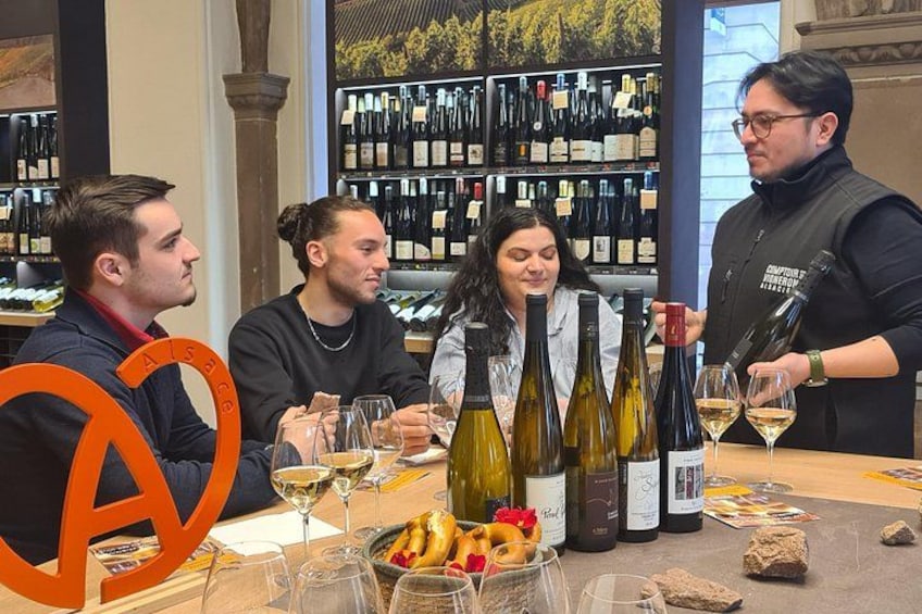 A group of people tasting wine at a table with various bottles and glasses. 2