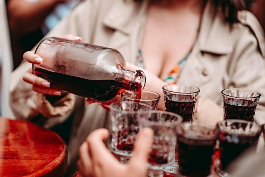 A person pouring a dark liquid from a bottle into several glasses. 3