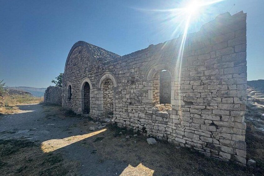 Un edificio de piedra con ventanas de arco y un techo parcialmente conservado, rodeado por un paisaje árido. 5