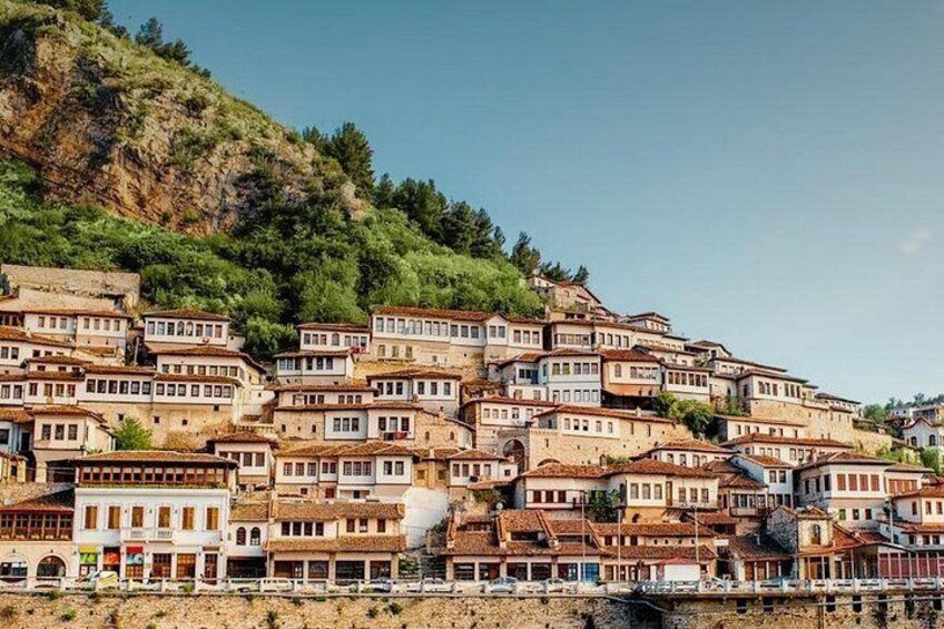 Un insediamento collinare con edifici a terrazze, cielo sereno e una distesa d'acqua alla base. 1
