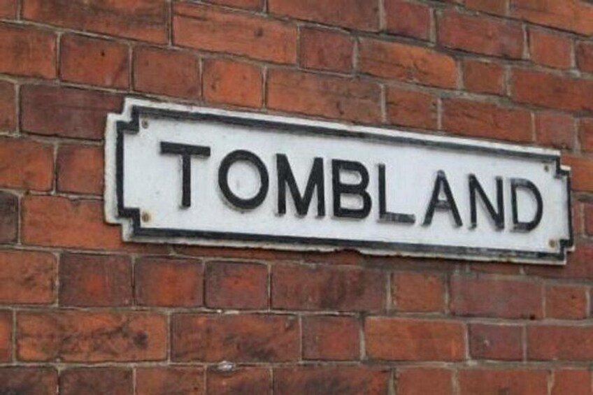 A street sign on a brick wall that reads 'TOMBLAND'. 2