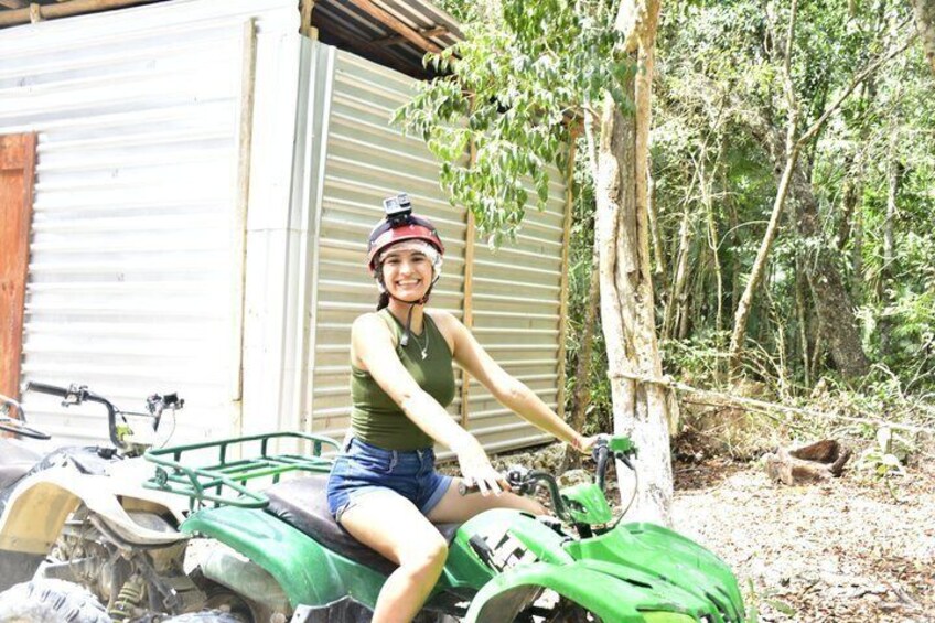 A person sitting on a green ATV in a rural setting with a metal shed and trees in the background. 4