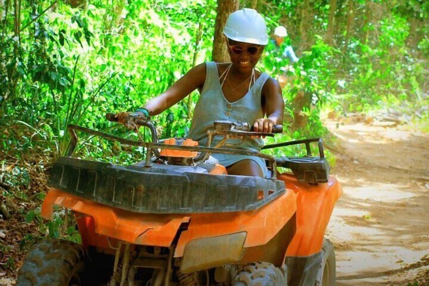 A person riding an orange ATV on a dirt path surrounded by greenery. 1