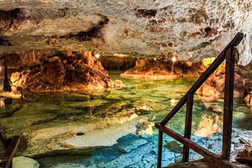 A cave interior with stalactites, a water pool, and a wooden staircase. 2