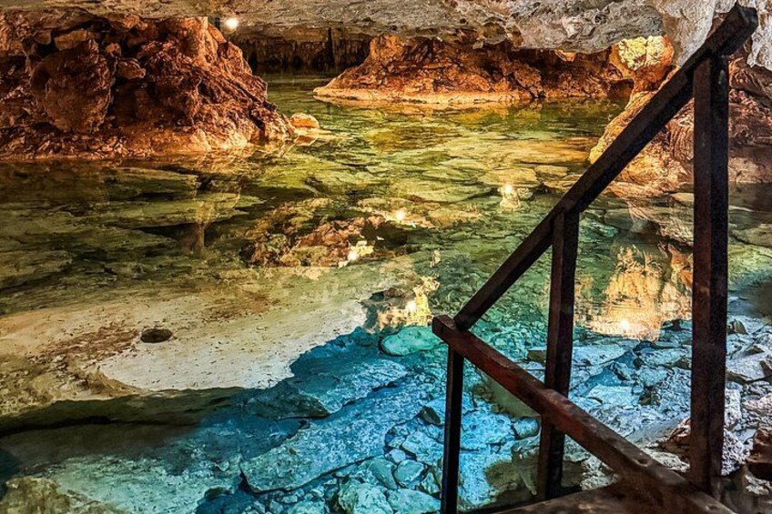 A cave with clear water, rocky formations, and a wooden staircase. 3