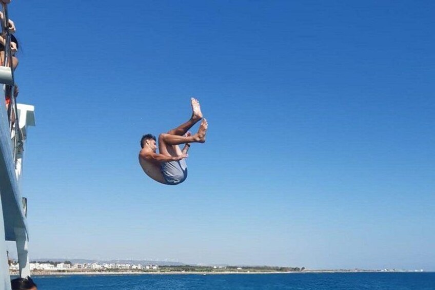 A person mid-diving with legs up, a clear blue sky, and a distant shoreline. 4