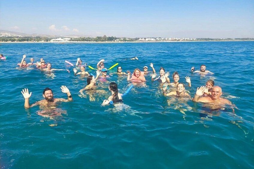 A group of people swimming in a body of water with a clear sky and distant buildings. 2