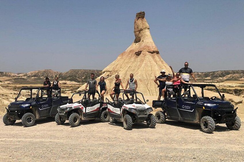 Off-road vehicles, a large rock formation, and a clear sky. 1