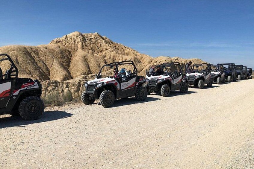 A row of ATVs parked on a dirt road with a large pile of sand in the background. 4