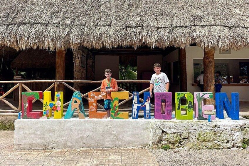 Un cartel junto a la playa con letras coloridas que dicen 'CHICHESTER BEACH' y dos personas de pie al frente. 4