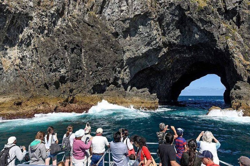 A group of people on a boat near a rocky coastline with a large natural arch formation. 2
