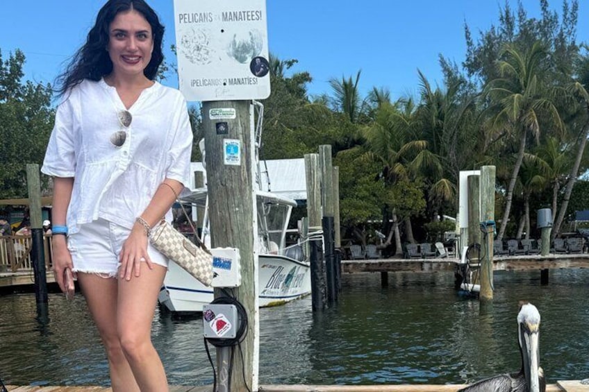 A woman standing by a dock with a sign that reads 'PELICAN & MANATEES.' 2