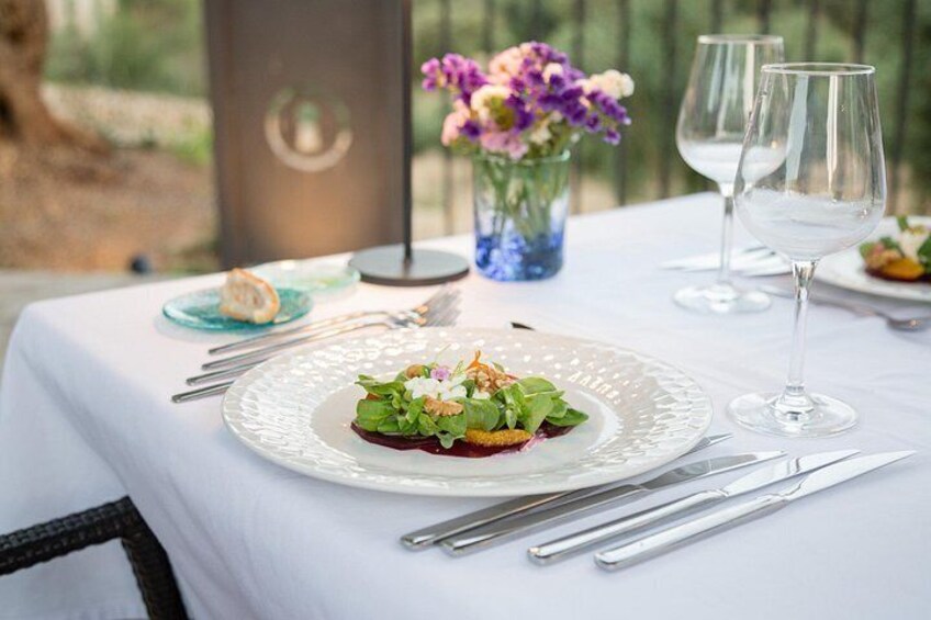 Une table dressée avec une nappe blanche, une assiette en verre contenant une salade et des verres à vin. 4