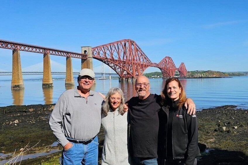 A group of people standing in front of a red bridge over water. 3