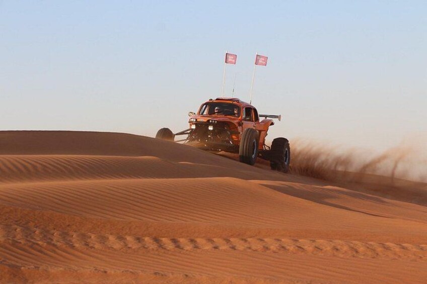 Un veicolo fuoristrada rosso che percorre un deserto con dune di sabbia e bandiere. 2