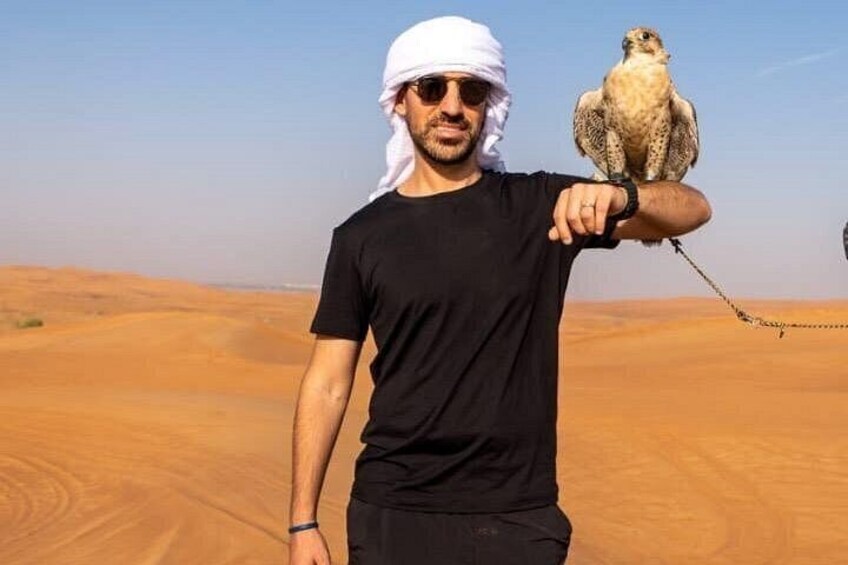 A person in a desert with a falcon perched on their arm. 3