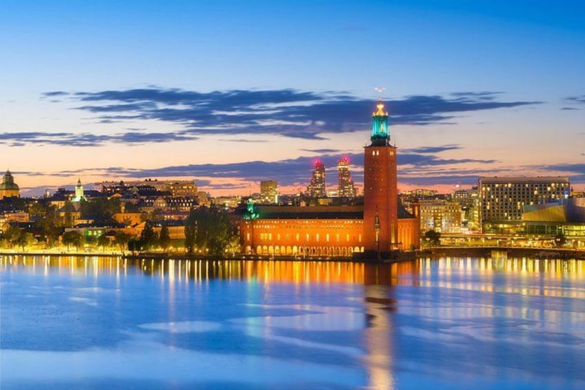 A cityscape at dusk with a prominent red building reflecting on calm water. 5
