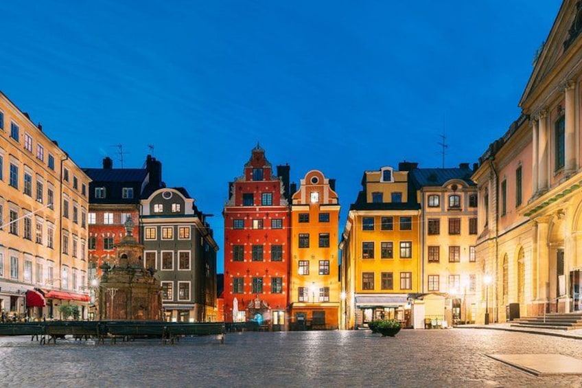 A cobblestone square with historic buildings, a fountain, and a clear evening sky. 2