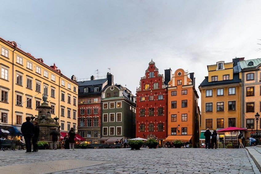 A cobblestone square with historic buildings, a fountain, and people walking. 3