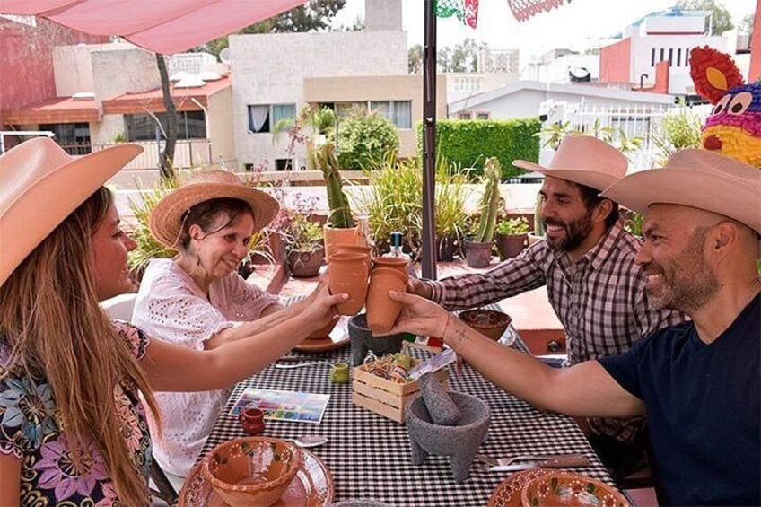 Un gruppo di persone sedute a un tavolo all'aperto, con vasi in terracotta, una tovaglia a quadri e una pianta di cactus. 1