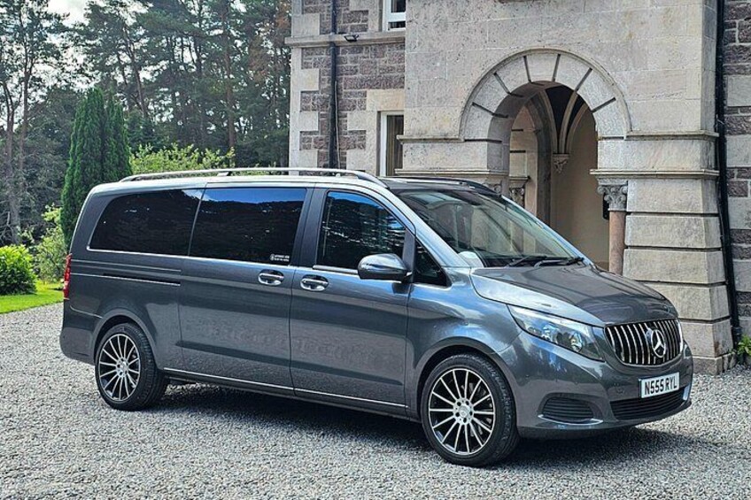 En grå Mercedes-Benz Sprinter varevogn parkeret foran en bygning i sten med buet indgang. 2