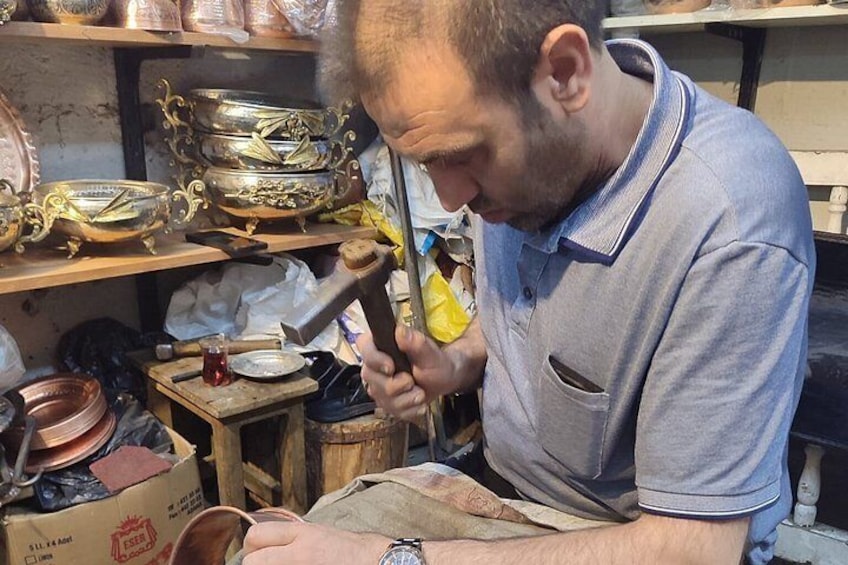 A person working with a hammer and a metal object, surrounded by various tools and metal containers. 4
