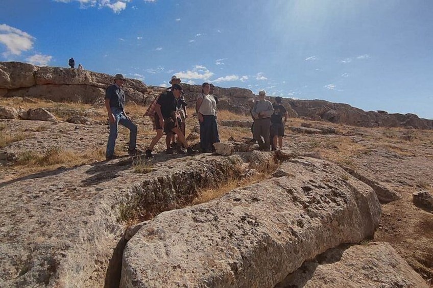 A group of people hiking on a rocky terrain with a large rock formation in the foreground. 3