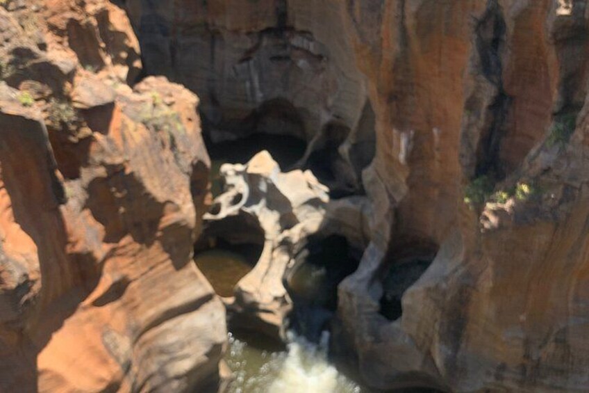 A canyon with a waterfall, rocky formations, and a small pool of water. 2
