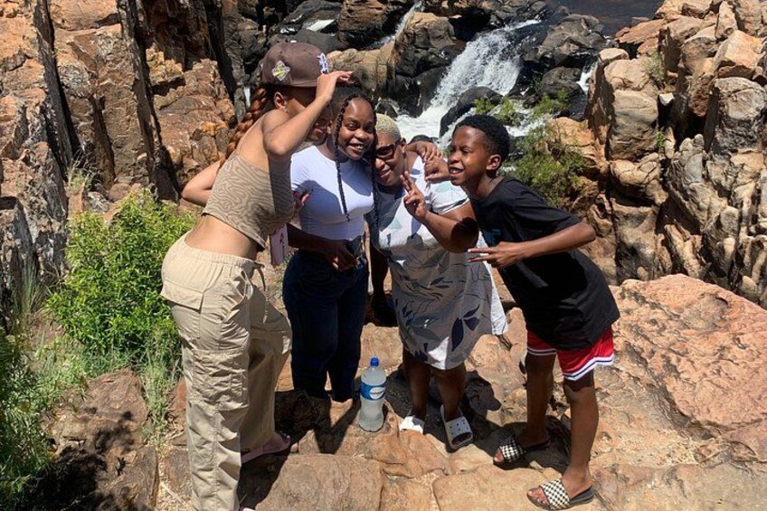 A group of people standing on rocky terrain with a waterfall in the background. 3