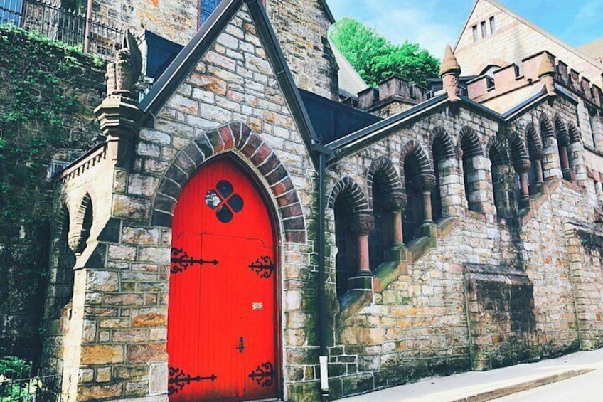 Une porte d’église rouge ornée d’une croix, des murs en pierre et une petite tour. 2