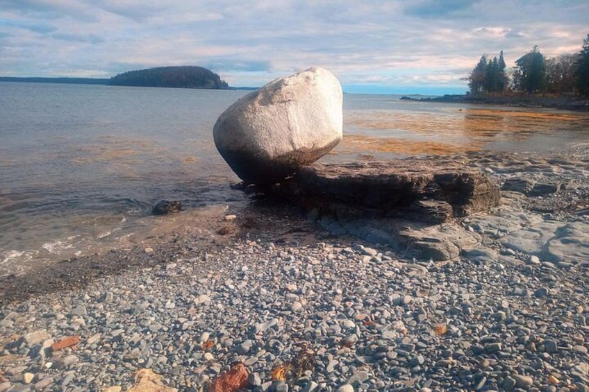 A pebble beach with a large rock in the foreground and a distant island. 2