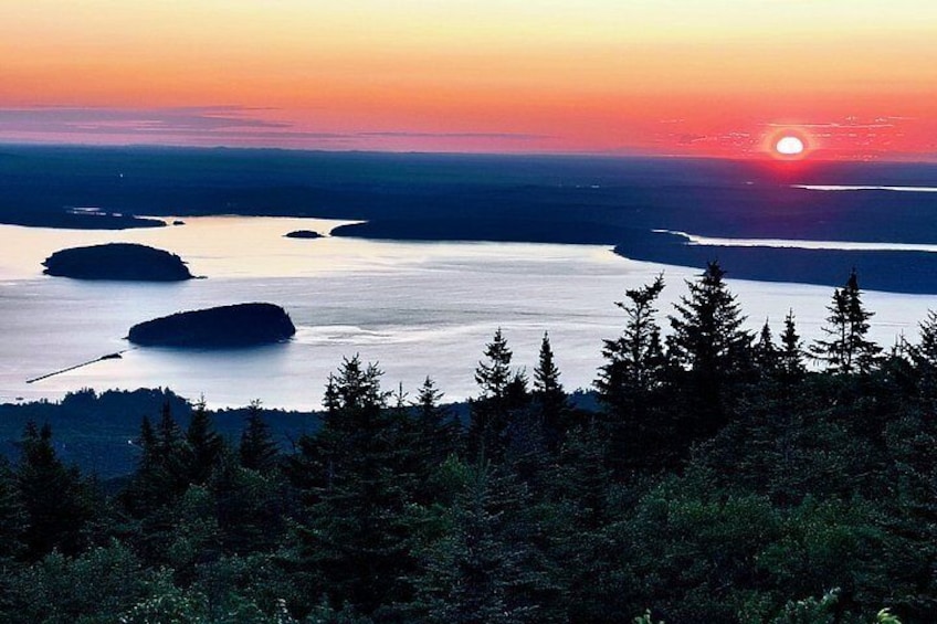 A sunset over a calm body of water with several islands, surrounded by dense forest. 3