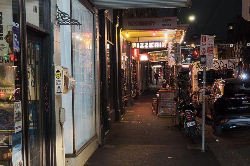 A narrow street with shops, including a pizza place, and parked motorcycles. 3