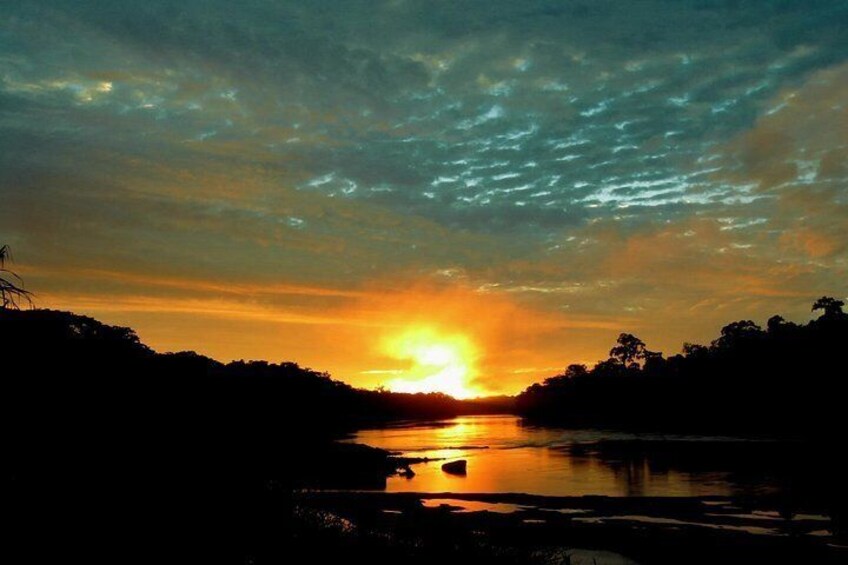 A sunset over a body of water with silhouettes of trees and a distant shoreline. 2