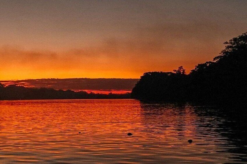 A sunset over a body of water with a silhouette of a tree-covered landmass in the background. 3