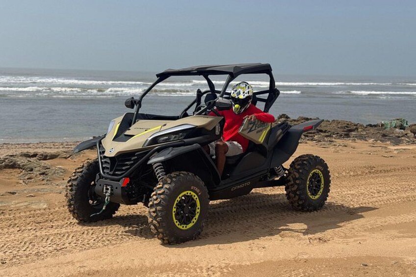 Een buggy rijdt op een zandstrand, met oceaan golven op de achtergrond. 1